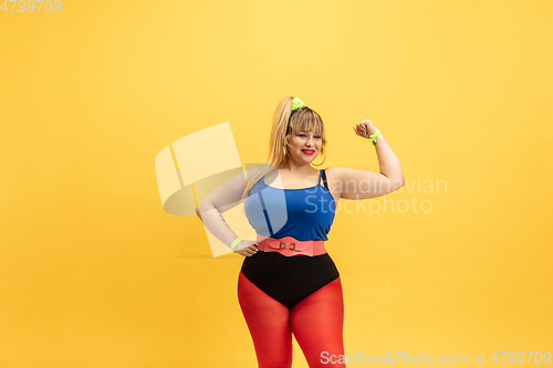 Image of Young caucasian plus size female model\'s training on yellow background