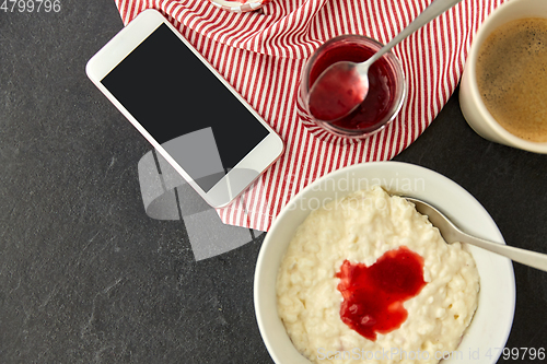 Image of porridge with jam, spoon, coffee and phone