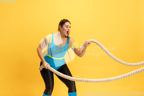 Image of Young caucasian plus size female model\'s training on yellow background