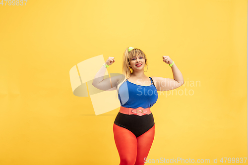 Image of Young caucasian plus size female model\'s training on yellow background