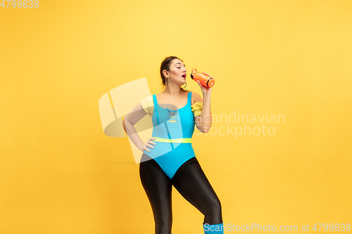Image of Young caucasian plus size female model\'s training on yellow background
