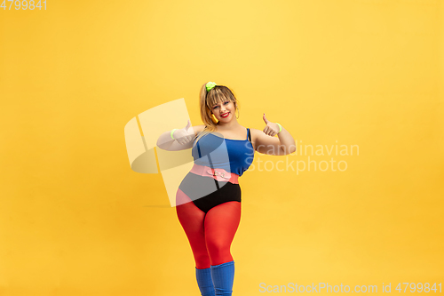 Image of Young caucasian plus size female model\'s training on yellow background