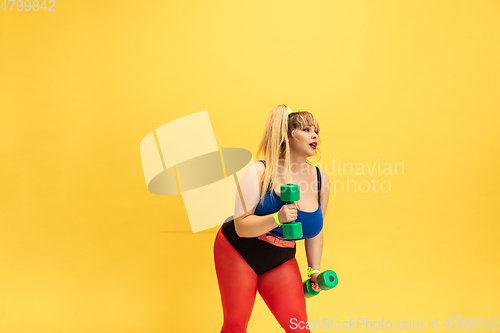 Image of Young caucasian plus size female model\'s training on yellow background