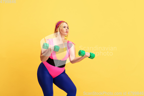 Image of Young caucasian plus size female model\'s training on yellow background