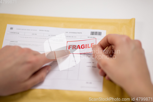 Image of hands sticking fragile marks to parcel in envelope