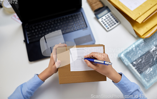 Image of close up of hands filling form on parcel at office