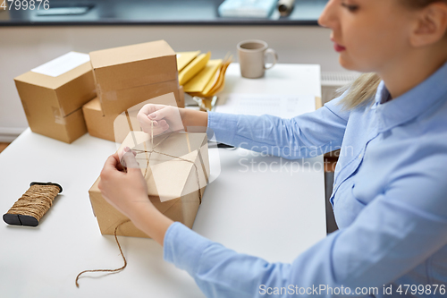 Image of woman packing parcel and tying rope at post office