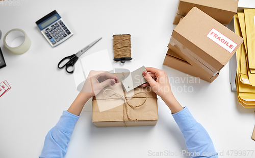 Image of hands tying name tag to parcel box at post office