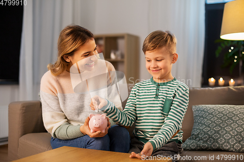 Image of mother and little son with piggy bank at home