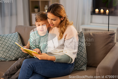 Image of happy mother and son reading book sofa at home