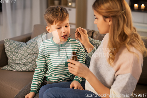 Image of mother giving medication or cough syrup to ill son