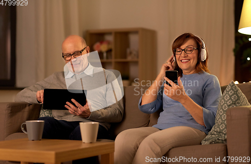 Image of happy senior couple with gadgets at home