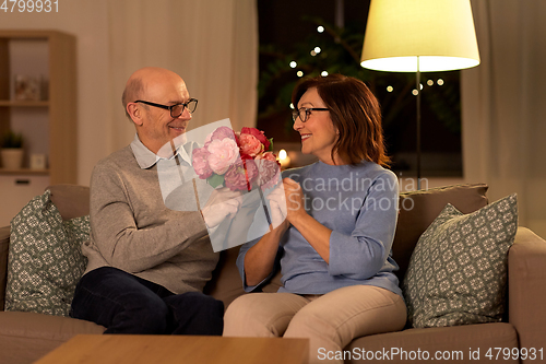 Image of happy senior couple with bunch of flowers at home