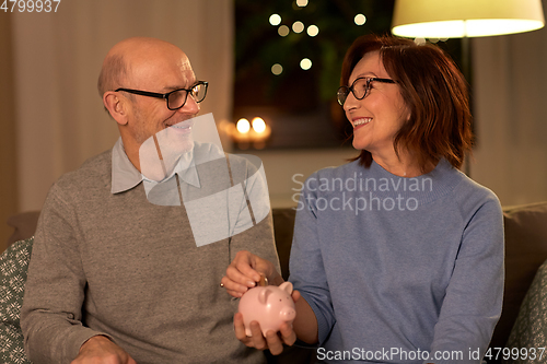 Image of happy senior couple with piggy bank at home