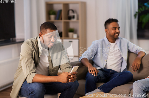 Image of man using smartphone while friends talking at home