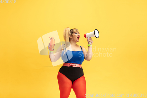 Image of Young caucasian plus size female model\'s training on yellow background