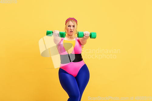 Image of Young caucasian plus size female model\'s training on yellow background