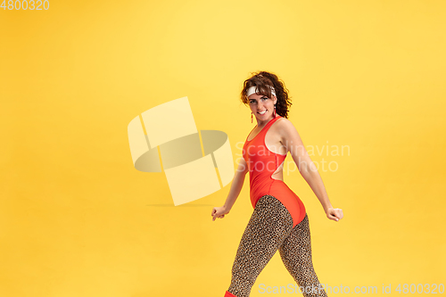 Image of Young caucasian plus size female model\'s training on yellow background