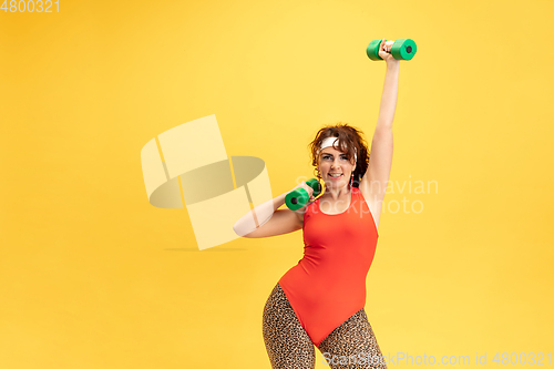 Image of Young caucasian plus size female model\'s training on yellow background