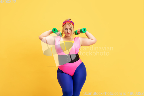 Image of Young caucasian plus size female model\'s training on yellow background