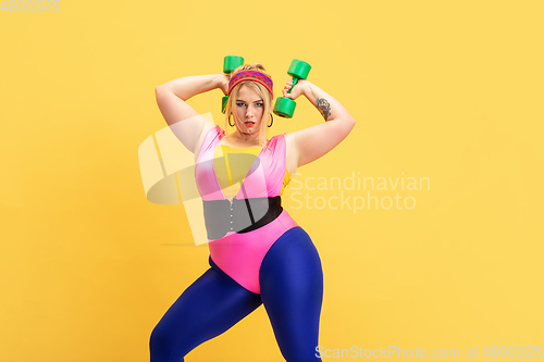 Image of Young caucasian plus size female model\'s training on yellow background