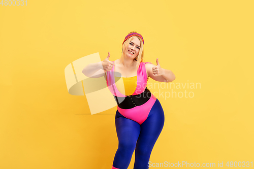 Image of Young caucasian plus size female model\'s training on yellow background