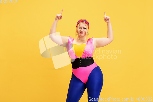 Image of Young caucasian plus size female model\'s training on yellow background