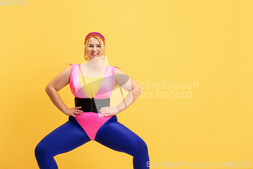 Image of Young caucasian plus size female model\'s training on yellow background