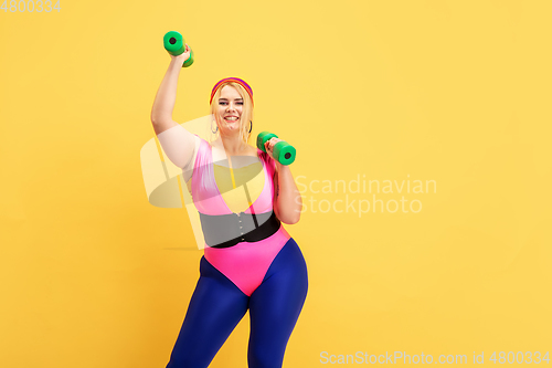 Image of Young caucasian plus size female model\'s training on yellow background