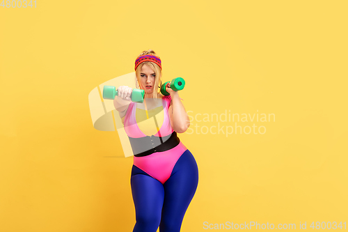 Image of Young caucasian plus size female model\'s training on yellow background