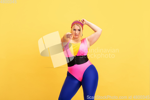 Image of Young caucasian plus size female model\'s training on yellow background