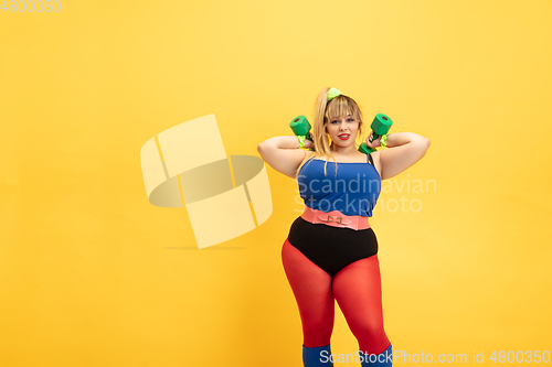 Image of Young caucasian plus size female model\'s training on yellow background
