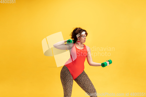 Image of Young caucasian plus size female model\'s training on yellow background