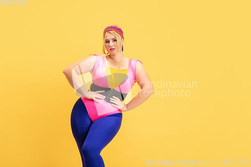 Image of Young caucasian plus size female model\'s training on yellow background