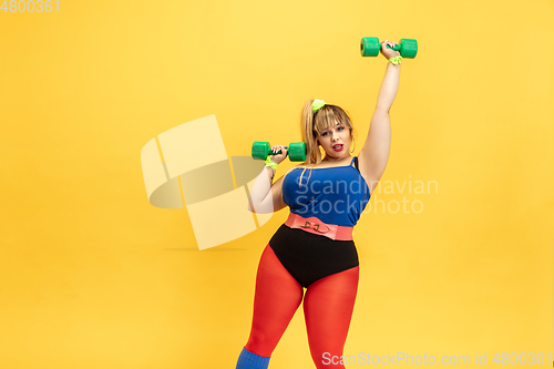 Image of Young caucasian plus size female model\'s training on yellow background