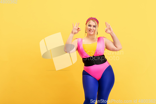 Image of Young caucasian plus size female model\'s training on yellow background