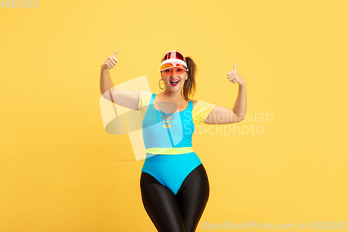 Image of Young caucasian plus size female model\'s training on yellow background