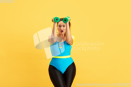 Image of Young caucasian plus size female model\'s training on yellow background