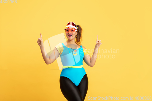 Image of Young caucasian plus size female model\'s training on yellow background