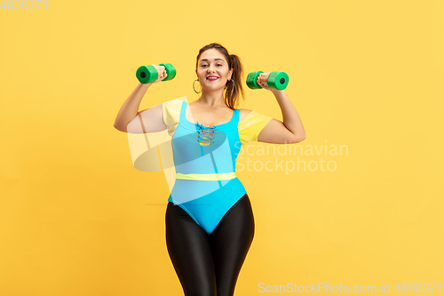 Image of Young caucasian plus size female model\'s training on yellow background