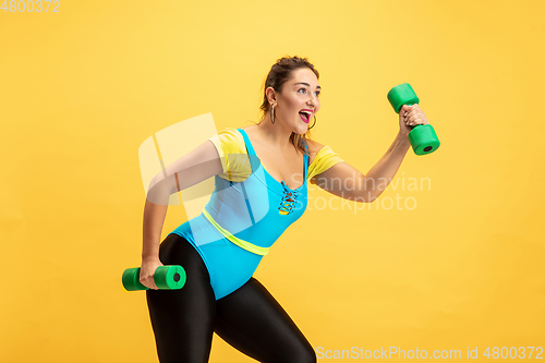 Image of Young caucasian plus size female model\'s training on yellow background