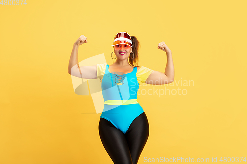 Image of Young caucasian plus size female model\'s training on yellow background
