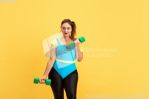 Image of Young caucasian plus size female model\'s training on yellow background