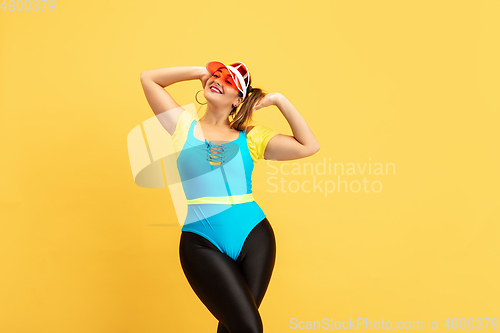 Image of Young caucasian plus size female model\'s training on yellow background