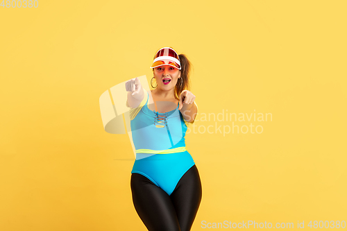 Image of Young caucasian plus size female model\'s training on yellow background