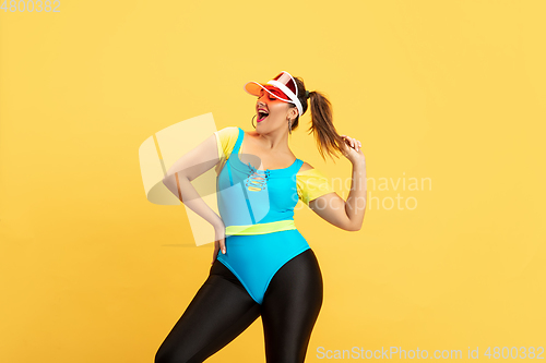 Image of Young caucasian plus size female model\'s training on yellow background