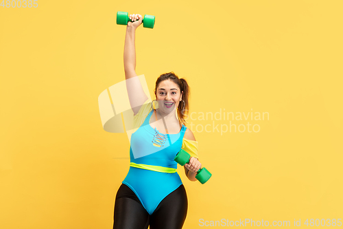 Image of Young caucasian plus size female model\'s training on yellow background