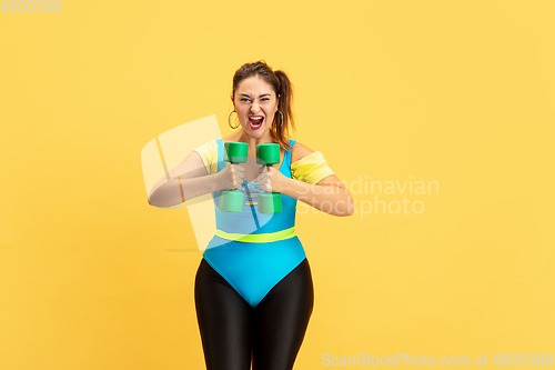 Image of Young caucasian plus size female model\'s training on yellow background