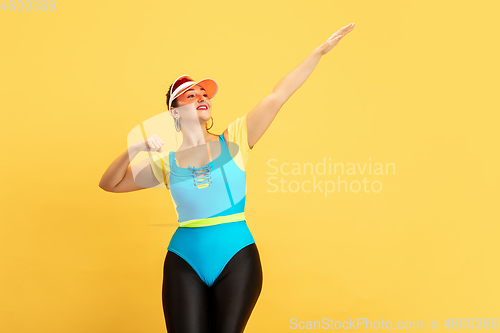 Image of Young caucasian plus size female model\'s training on yellow background