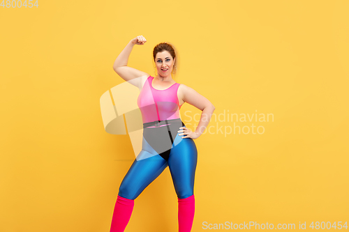 Image of Young caucasian plus size female model\'s training on yellow background